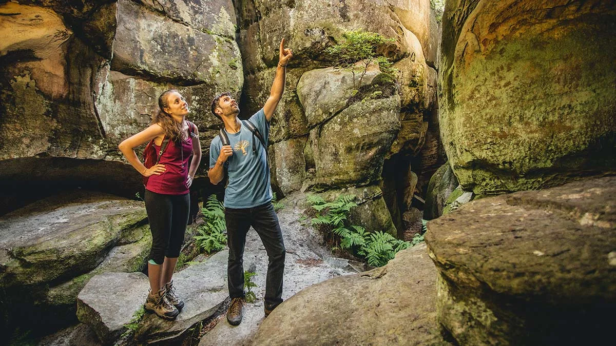 Two hikers exploring narrow sandstone passages between giant boulders at Great Channels Natural Area Preserve