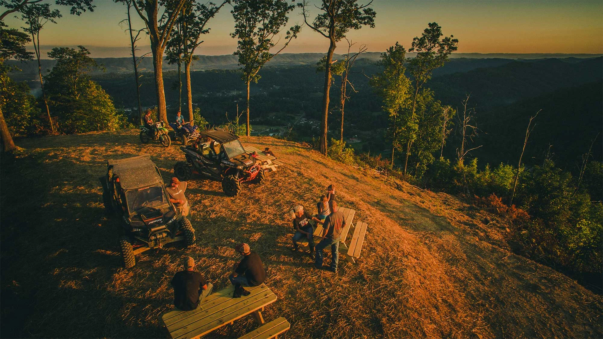 Group of off-road riders with UTVs and dirt bikes gathered at a Spearhead Trails overlook at sunset