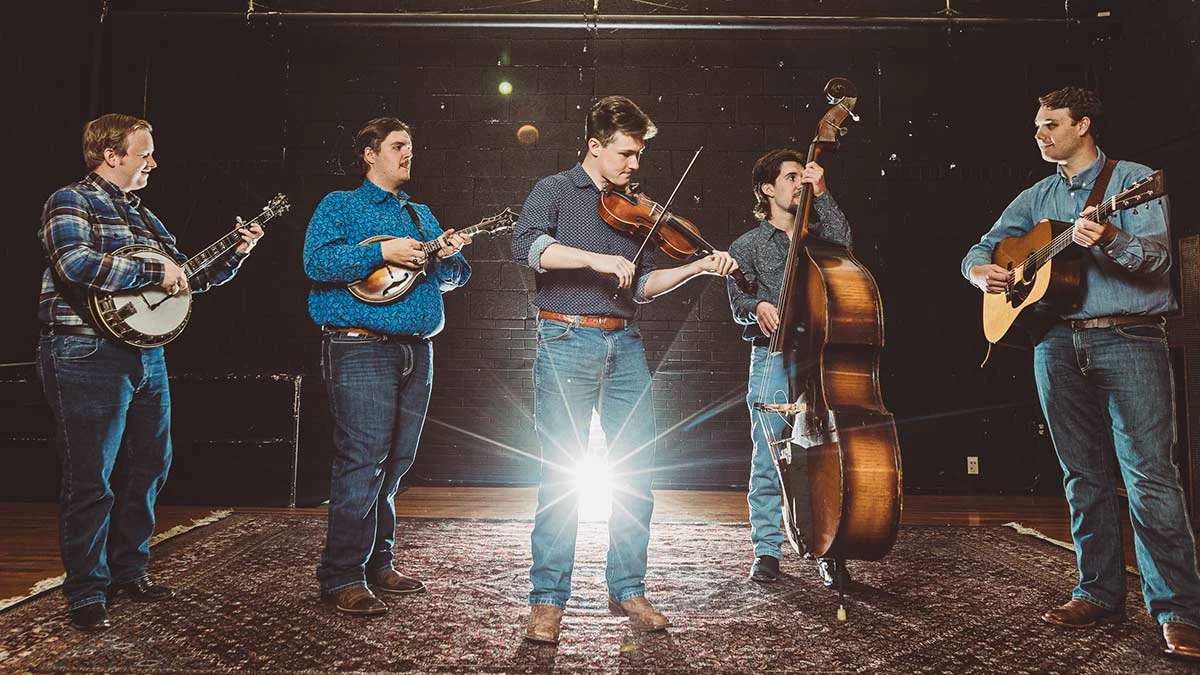 Five-piece bluegrass band with banjo, mandolin, fiddle, bass, and guitar performing on stage