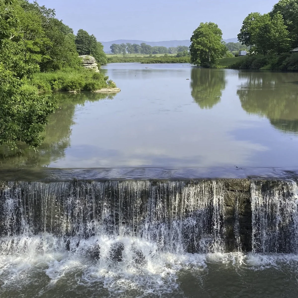 Burke's Garden Dam, a low waterfall spilling over a stone ledge with distant mountains in Tazewell County, Virginia