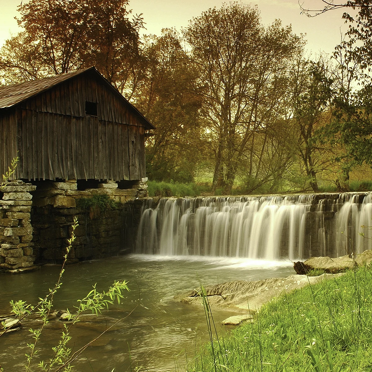 The weathered wooden Cowan Mill on a stone foundation above a wide waterfall dam near Ewing in Lee County, Virginia
