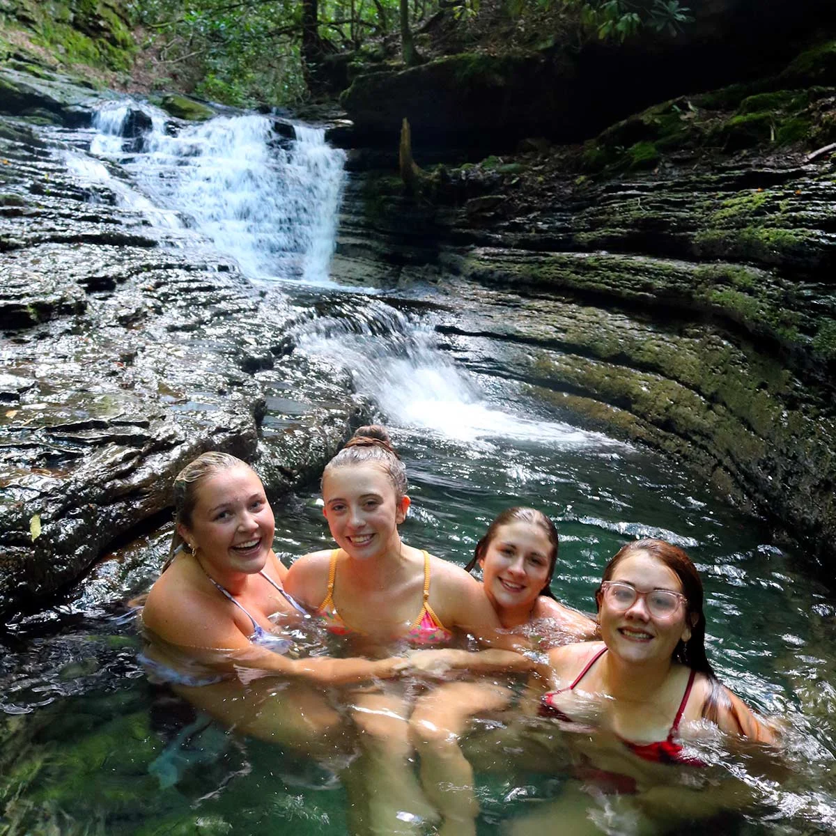 Four friends swimming in the clear pool below the falls at Devil's Bathtub in Scott County, Virginia.