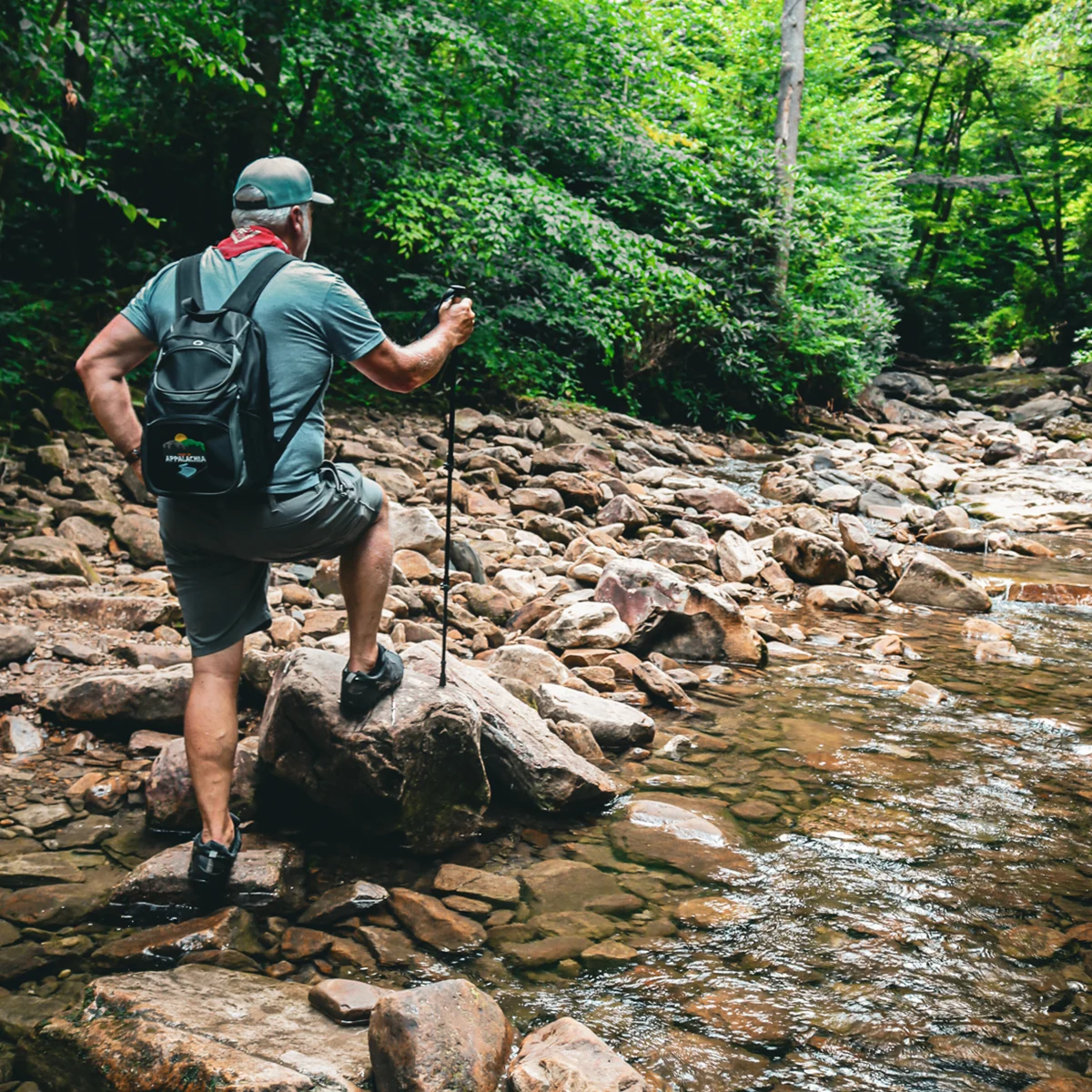 Hiker with trekking pole and backpack crossing a rocky creek along the Devil's Fork Trail to the Devil's Bathtub in Scott County, Virginia