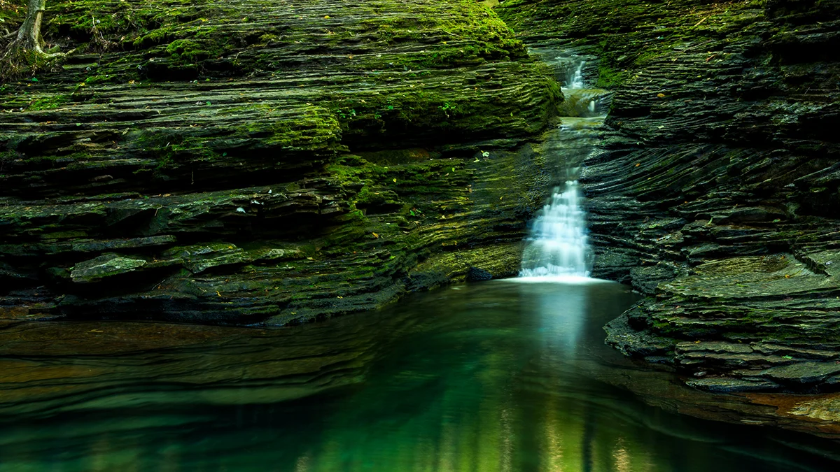 Waterfall cascading into the deep emerald pool of the Devil's Bathtub framed by mossy layered rock in Scott County, Virginia