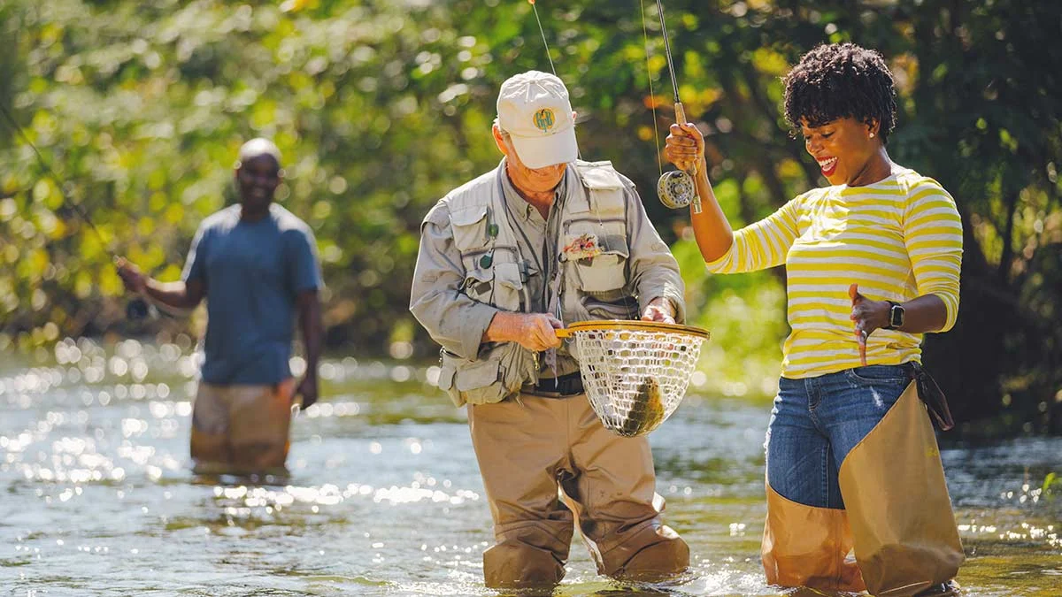 Two anglers fly fishing in a river, one holding a net with a caught fish, in Southwest Virginia