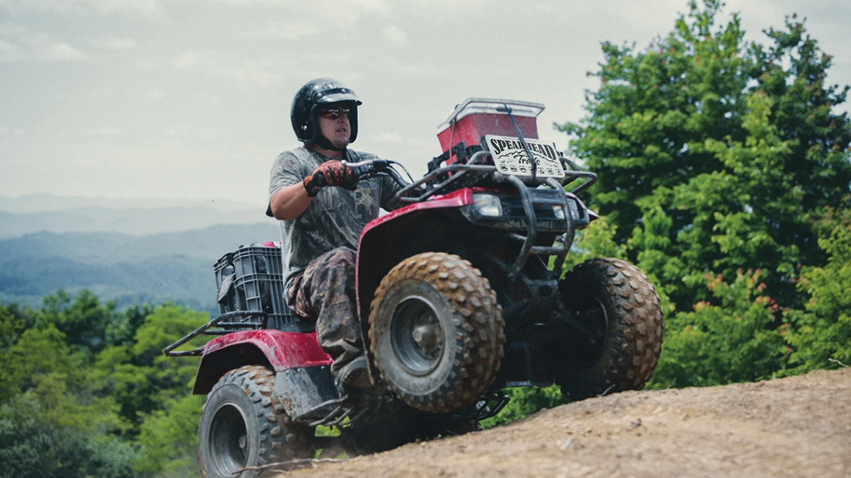 four-wheeler-atv-riding-spearhead-trails-virginia.jpg A rider navigates a red ATV featuring a Spearhead Trails logo plate up a steep dirt incline with mountain ranges in the background.