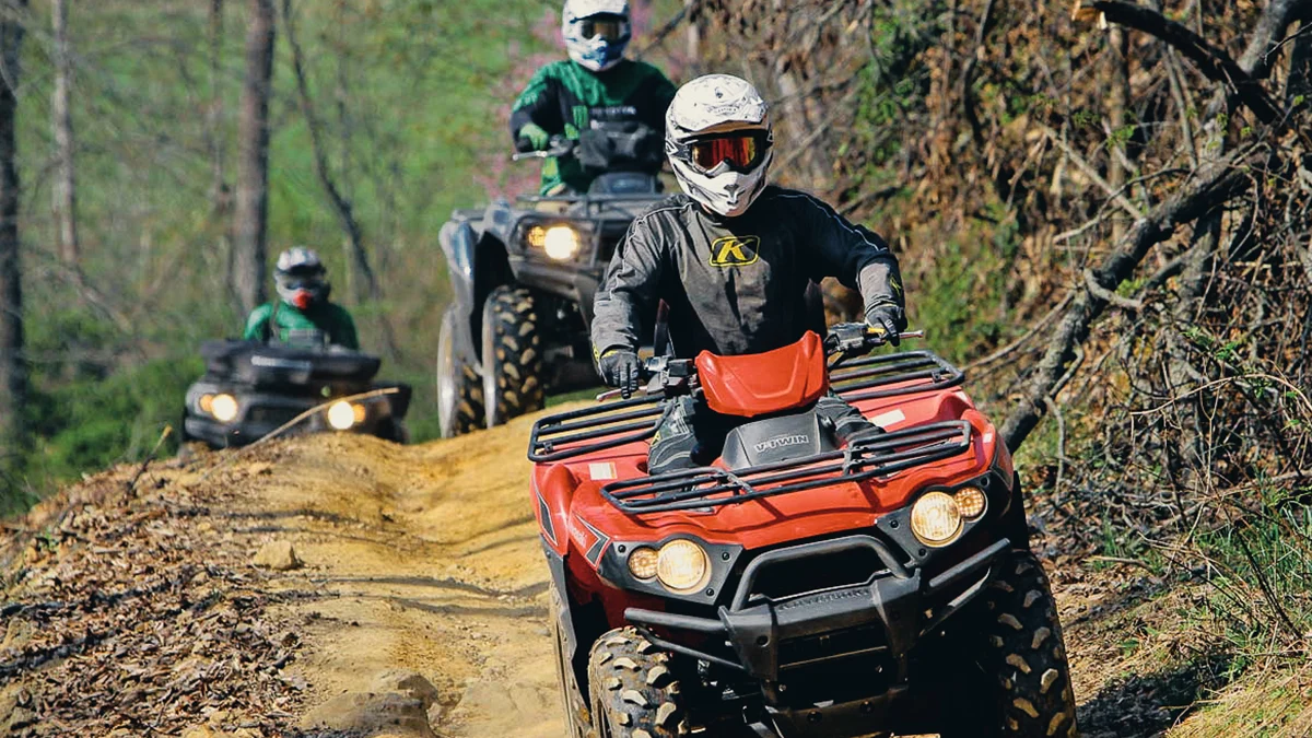 group-atv-riders-stone-mountain-trail-spearhead-trials-virginia.jpg A lineup of off-road riders on ATVs wearing full-face helmets riding down a winding dirt trail in the Stone Mountain Trail System of Virginia.