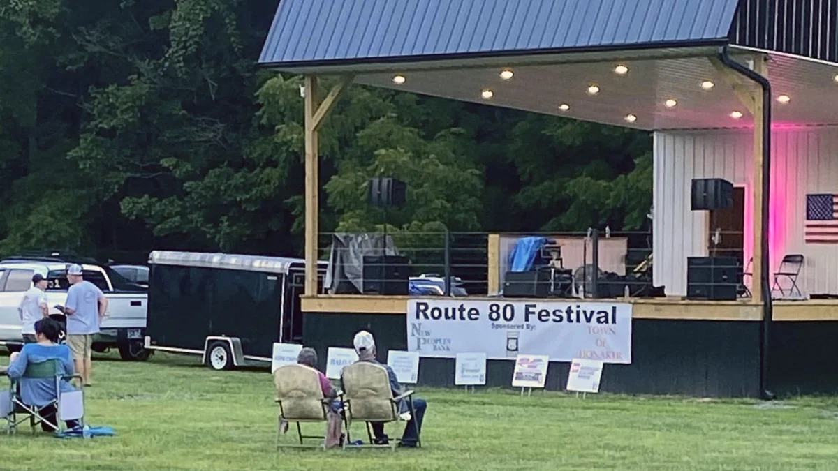 A small crowd in lawn chairs watches a covered outdoor stage with a "Route 80 Festival" banner in Honaker, Virginia.