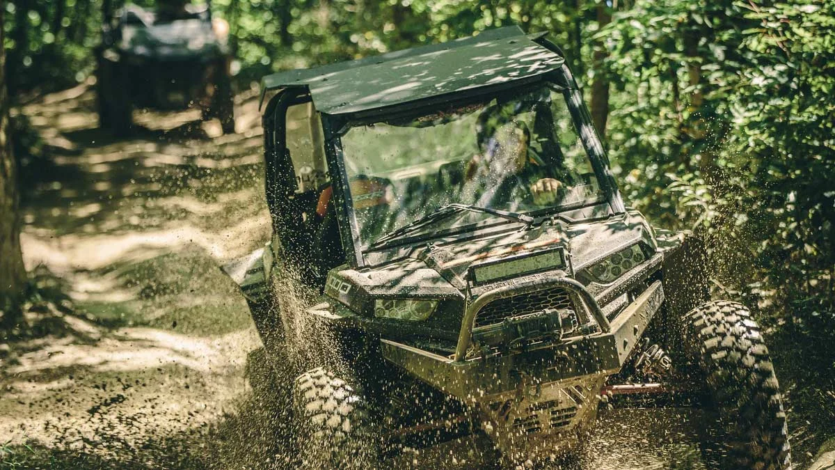 utv-splashing-mud-wooded-offroad-trail-virginia.jpg An action shot of an off-road side-by-side UTV kicking up mud and water as it navigates a rugged, wooded trail in Virginia.