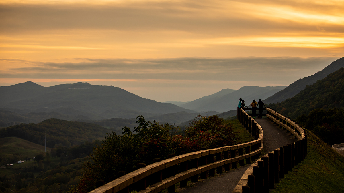 Visitors at a split-rail overlook watch the sunset over Powell Valley's layered ridges in Wise County, Virginia