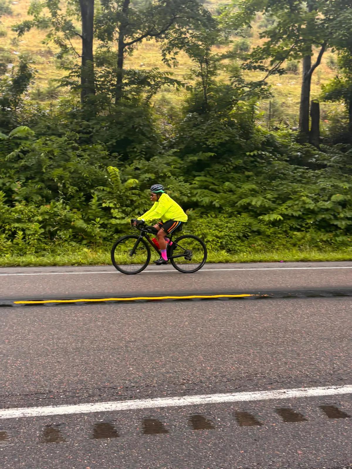 Two cyclists stopped together on a wet paved road, one wearing a neon yellow jacket